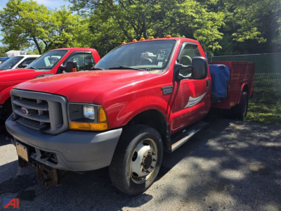 Red 2001 Ford F-550 Super Duty utility truck in a parking lot, front-left view with black grille, gray bumper, single cab, utility bed behind cab, other red trucks in background.