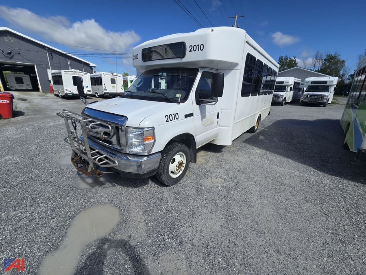 Ford E450 wheelchair bus with front hitch and 2010 labeling, side windows, multiple similar buses in a lot.