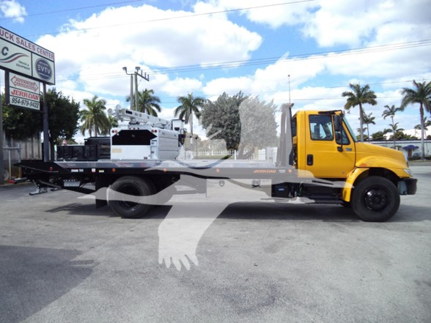 2019 International Durastar 4300 rollback truck with yellow cab and flatbed rear, side view showing equipment on the bed and hydraulic systems.