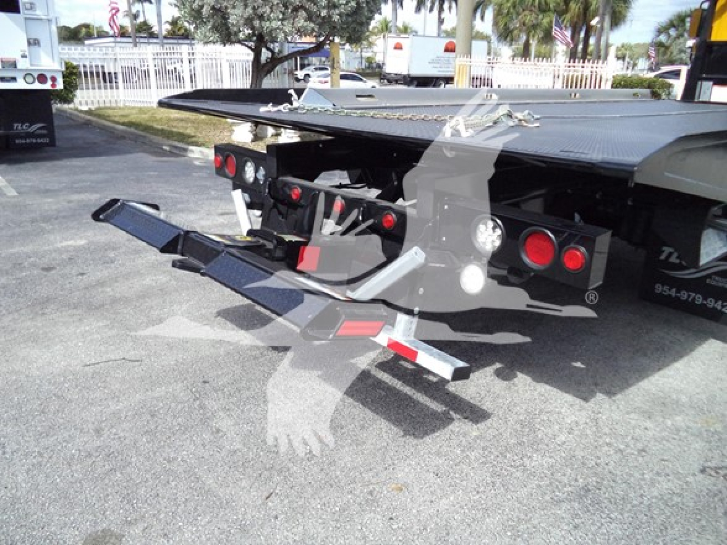 Truck bed with hydraulic rollback mechanism extended, taillights and reflective safety bars visible under the platform, International Durastar 4300 rear view.