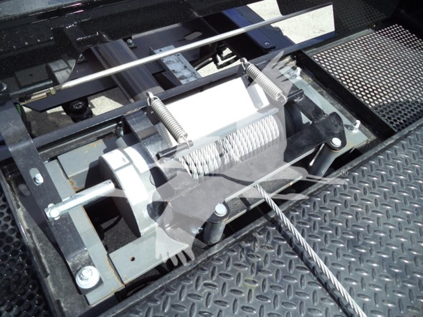 Truck rollback winch mechanism with steel cable and coiled drum showing on diamond plate bed