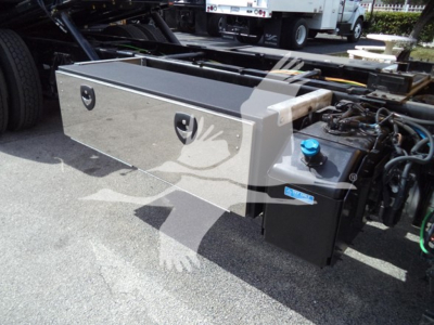 Side view of a 2019 International Durastar 4300 rollback truck showing a long aluminum toolbox mounted beside the cab and a blue fluid fill cap on the hydraulic reservoir.