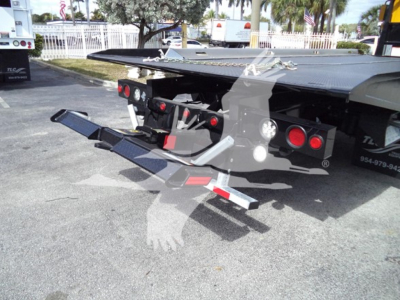 Truck bed with hydraulic rollback mechanism extended, taillights and reflective safety bars visible under the platform, International Durastar 4300 rear view.