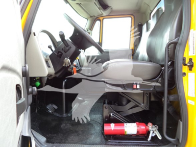 Truck cab interior of a 2019 International Durastar 4300 rollback showing steering wheel, dashboard, driver seat, and firewall with a red fire extinguisher on the floor near the pedals.