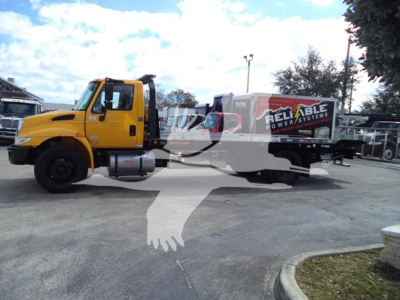 Truck cab and rollback bed in yellow International Durastar 4300 with visible 'Reliable Power Systems' branding on equipment trailer.