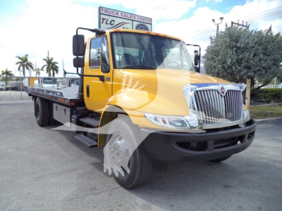 Truck bed tow truck in yellow International Durastar cab front view showing flatbed and chrome grille.