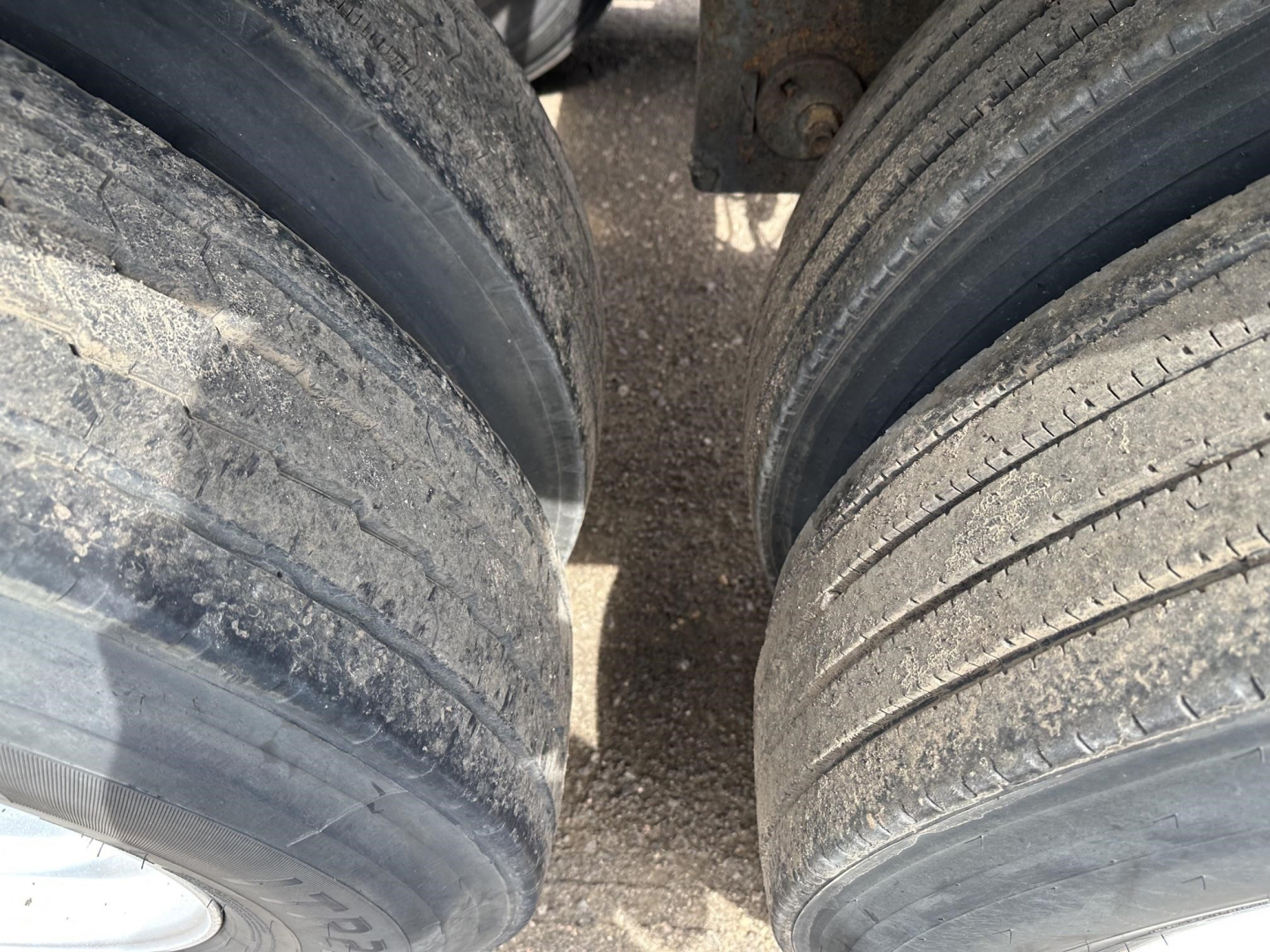 Trailer dual rear wheels with visible tread and dirt, close-up view of tire sidewalls and gaps between wheels.