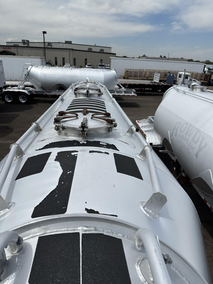 Top view of a Polar Gravity Drop Pneumatic trailer tank showing manhole/valve assembly on top, access hatches, and shiny silver surface with black rectangular graphics.