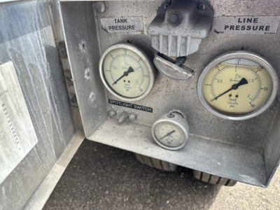Pneumatic trailer control panel with two pressure gauges labeled Tank Pressure and Line Pressure, a small switch label Spotlight, a relief valve, and a central knob; metal panel with weathered finish.