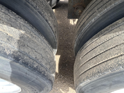 Trailer dual rear wheels with visible tread and dirt, close-up view of tire sidewalls and gaps between wheels.