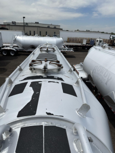 Top view of a Polar Gravity Drop Pneumatic trailer tank showing manhole/valve assembly on top, access hatches, and shiny silver surface with black rectangular graphics.