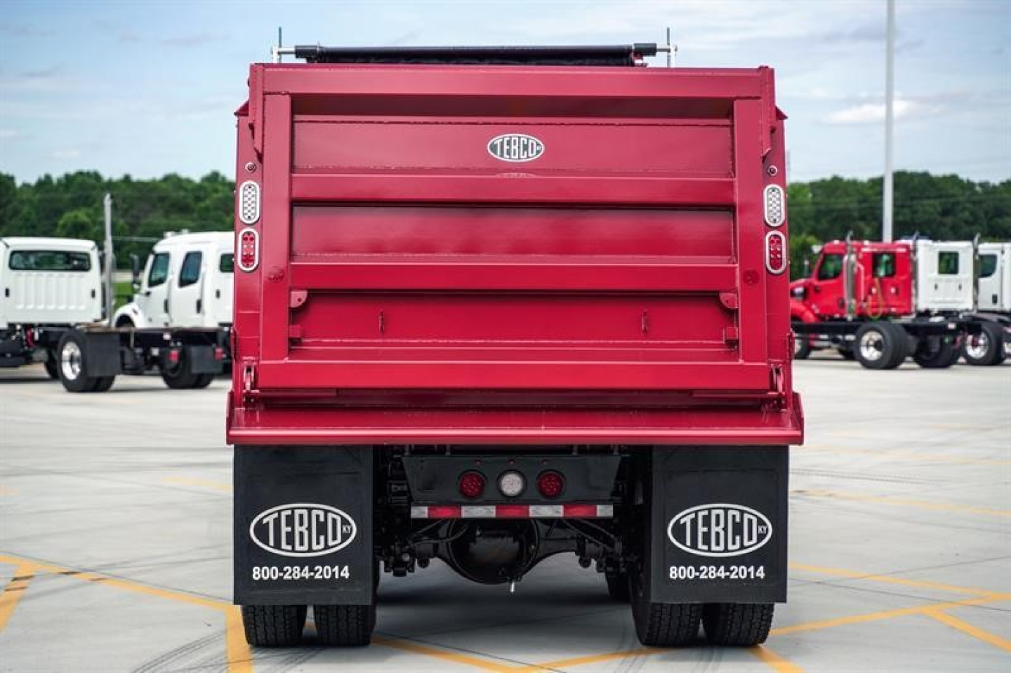 Rear view of a red dump truck bed with TEBCO mud flaps and dual rear tires, showing the tailgate and hydraulic components.