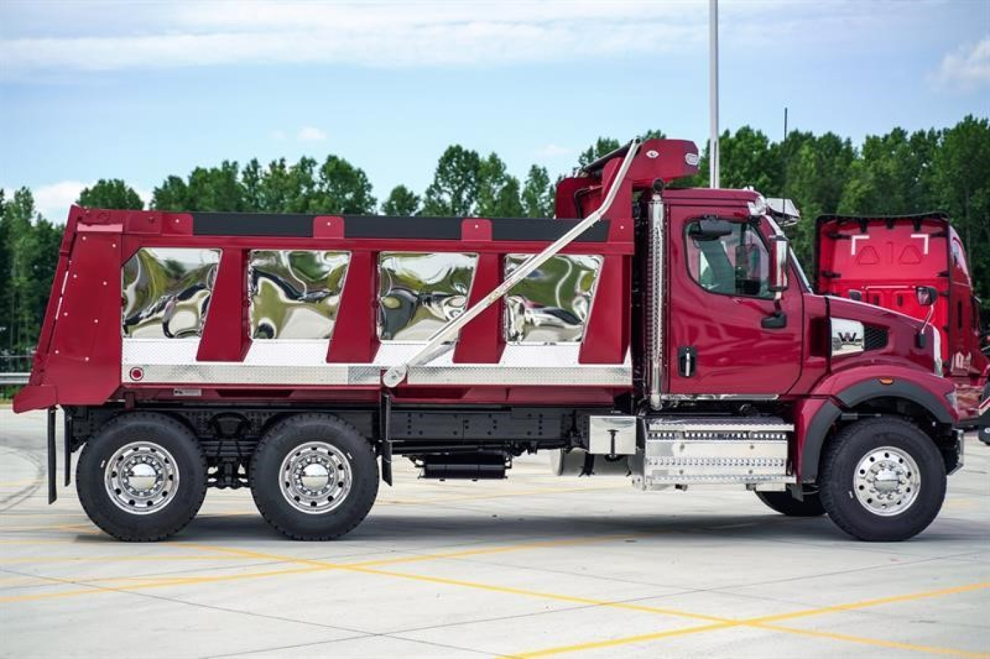 New Western Star 47X dump truck in red with chrome accents and dump bed. Side view showing three-axle configuration and brand badge on cab.