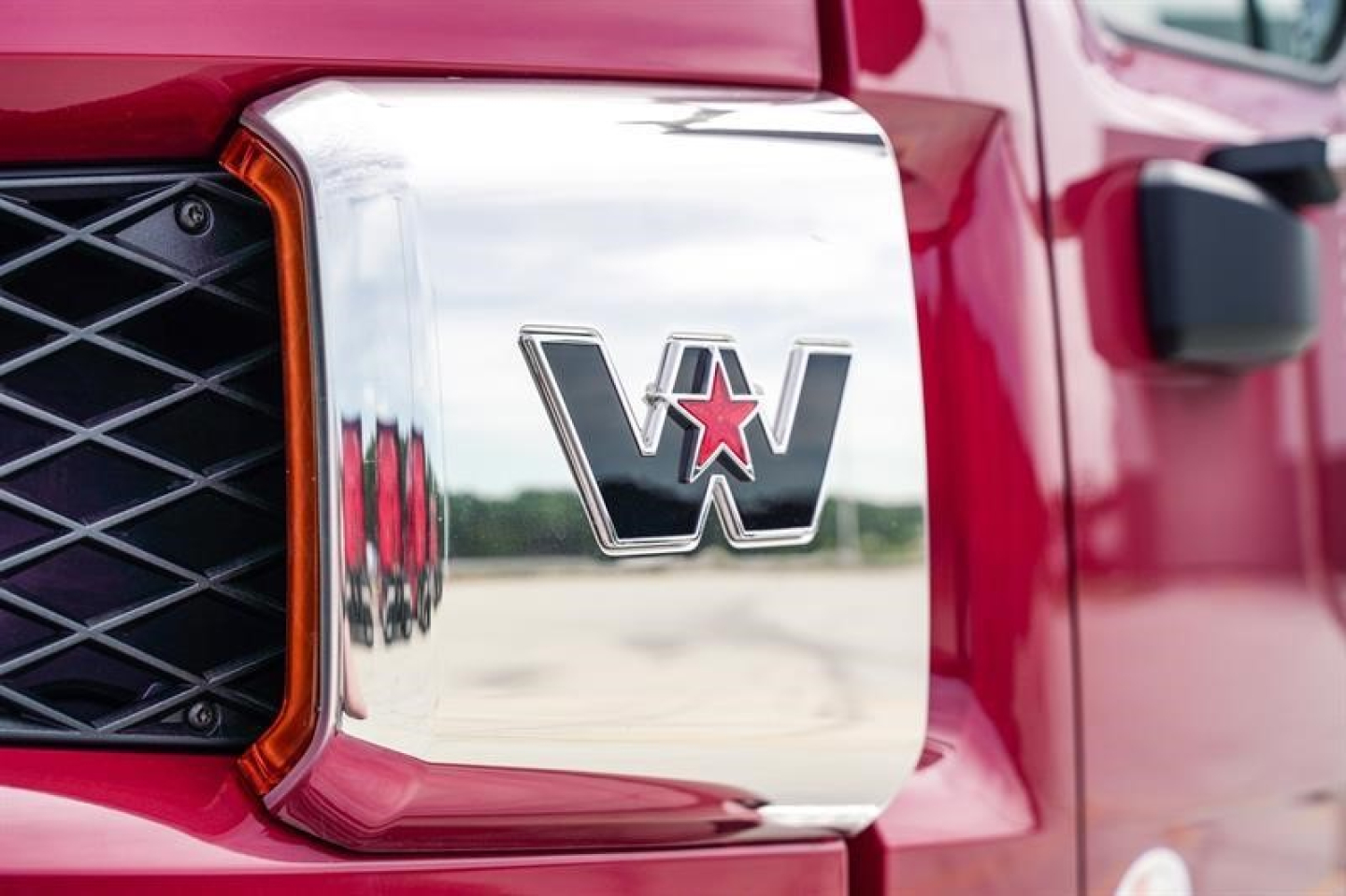 Truck front grille and emblem close-up showing a chrome 'W' logo with a red star, on a red Western Star 47X truck.