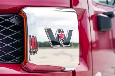 Truck front grille and emblem close-up showing a chrome 'W' logo with a red star, on a red Western Star 47X truck.