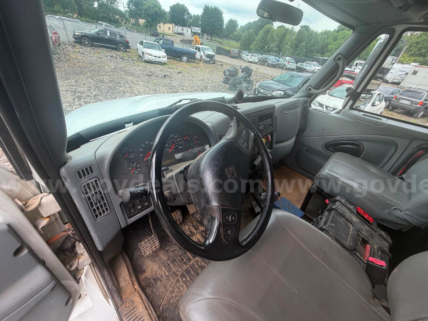 Truck cab interior of a 2004 International 4300 showing steering wheel, dashboard, and grey seats; dirt on floor mat.