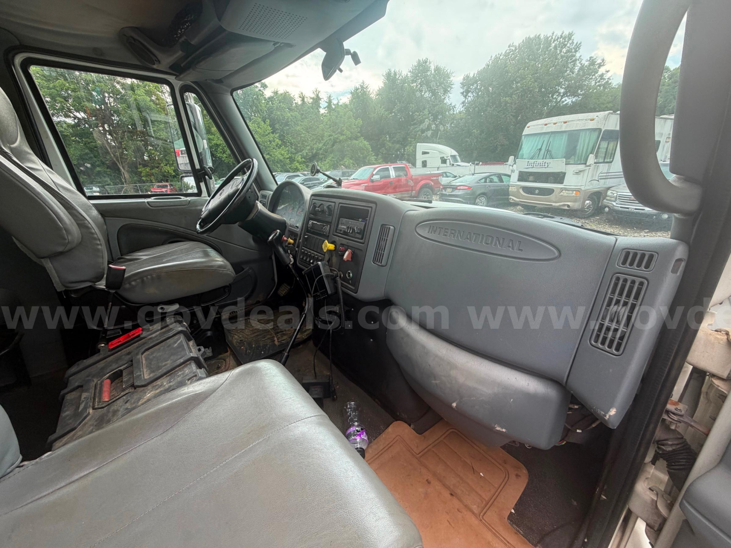 Cab interior of a 2004 International 4300 tow truck showing dashboard, steering wheel, and passenger seat with visible controls and equipment on the center console.