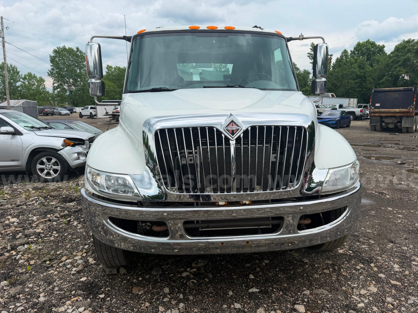 Front view of a white 2004 International 4300 tow truck showing chrome grille, bumper, and badge, with side mirrors and orange clearance lights.