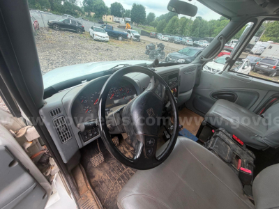 Truck cab interior of a 2004 International 4300 showing steering wheel, dashboard, and grey seats; dirt on floor mat.
