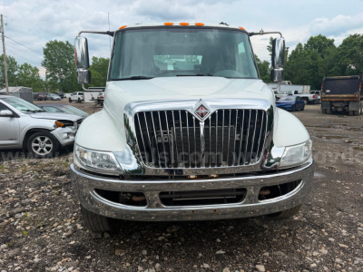 Front view of a white 2004 International 4300 tow truck showing chrome grille, bumper, and badge, with side mirrors and orange clearance lights.