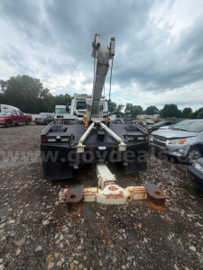 Tow truck hook arm and hitch assembly mounted on a flatbed, rear view showing rusted hitch receiver and hydraulic boom in raised position.