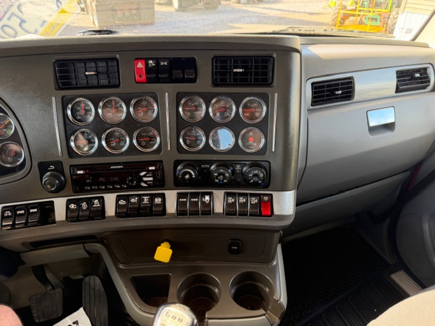 Dashboard interior of a 2017 Kenworth T880 showing multiple gauges and controls; center console with switches, two cup holders, yellow key tag in slot.