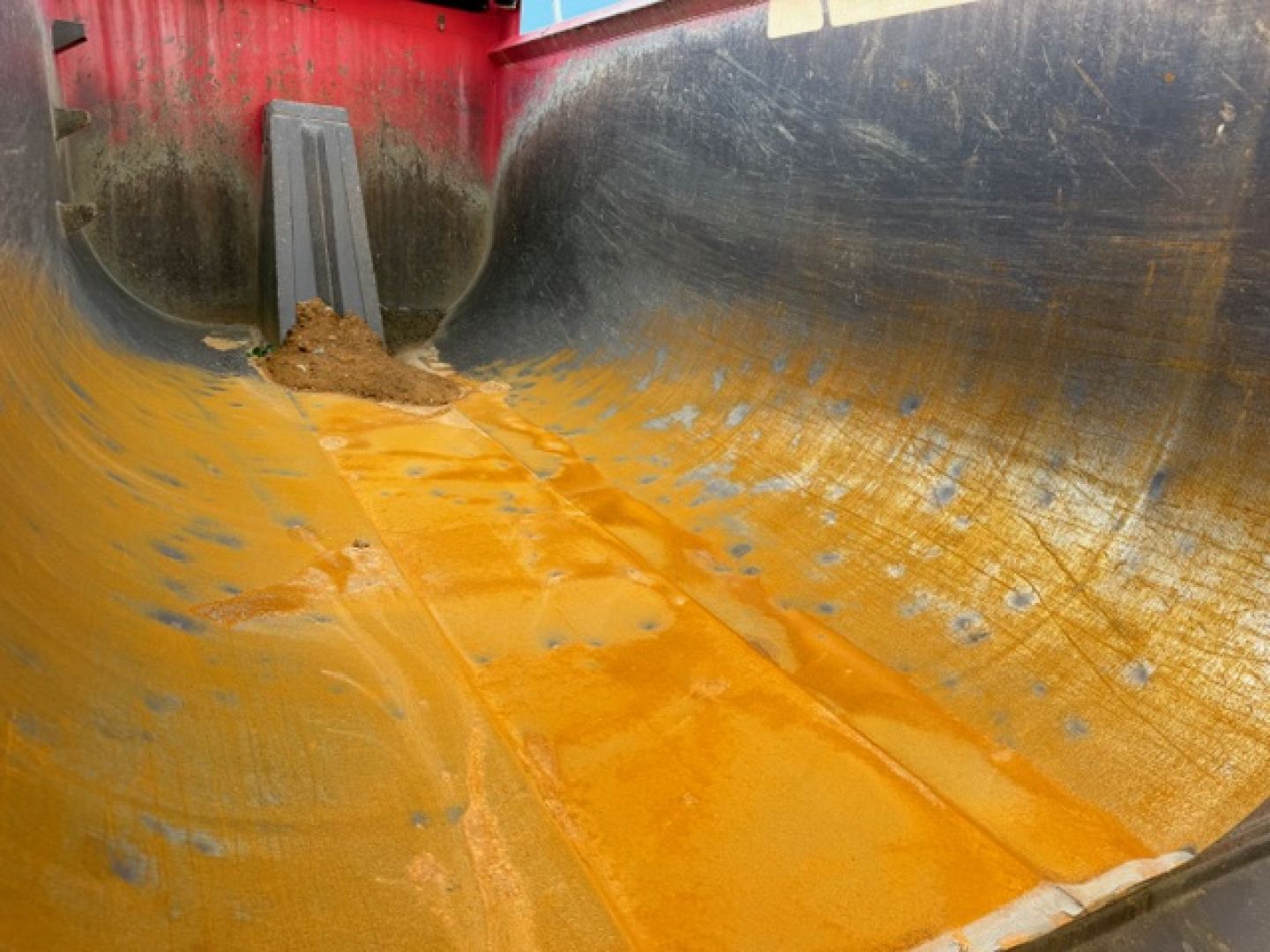 Dump bed interior of a Kenworth T880 showing orange bed liner and spray-on coating with dirt and scuff marks.