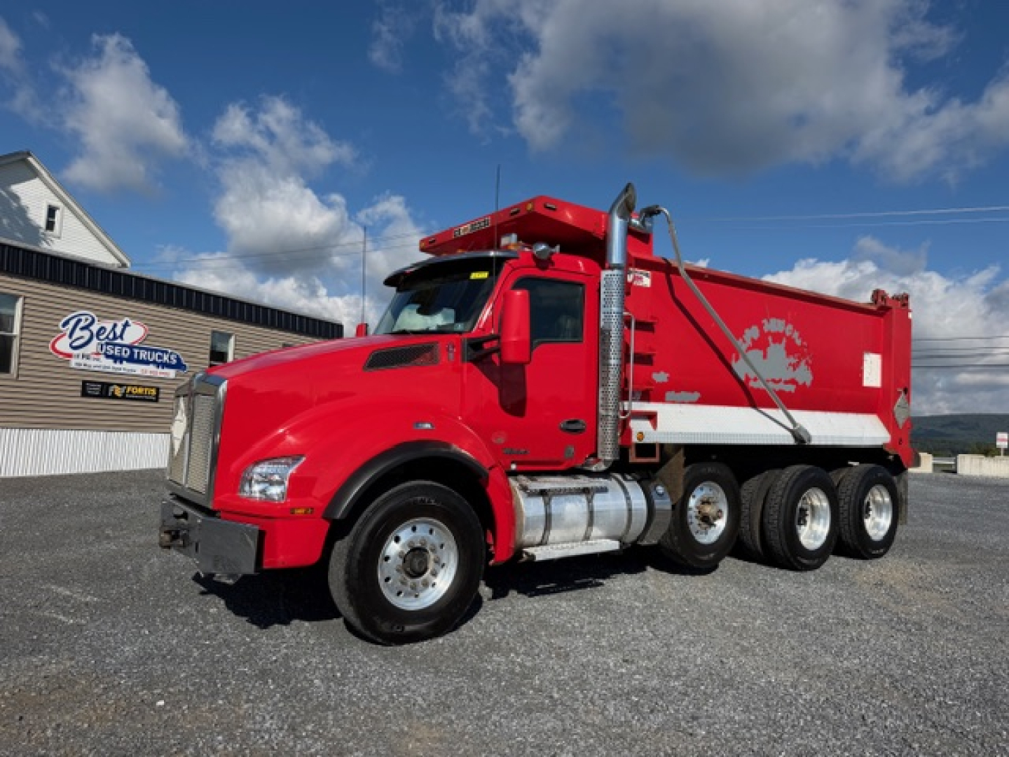 Kenworth T880 dump truck in red with white dump body, side view showing fuel tanks and wheels.