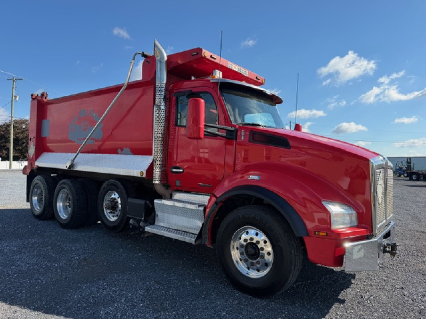Kenworth T880 dump truck, red cab and dump body, side view showing chrome front bumper, dual rear axles, and PTO under cab.