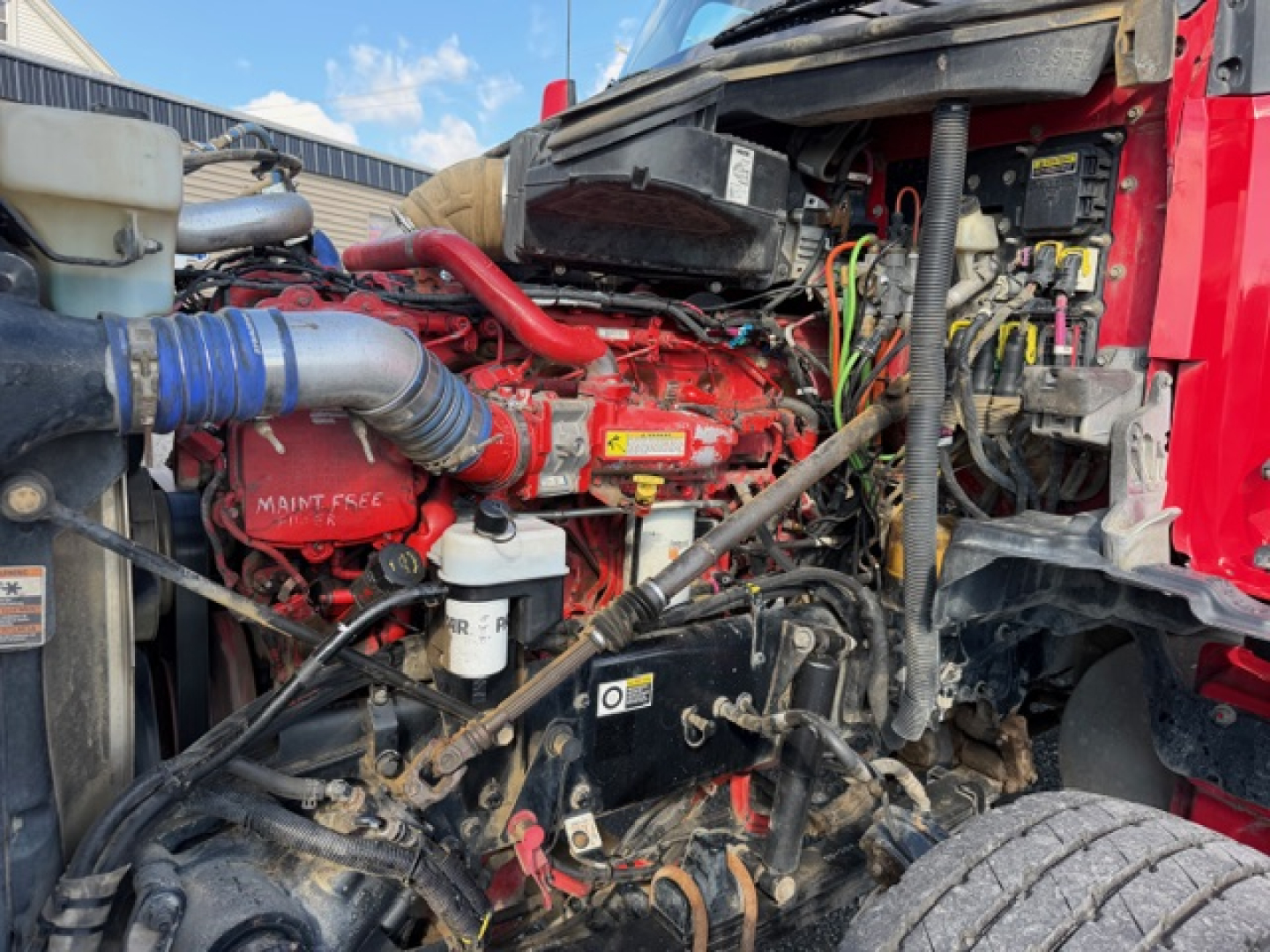 Kenworth T880 engine bay with red engine, hoses, and wiring; visible coolant reservoir, air intake, and various components in front/right view.