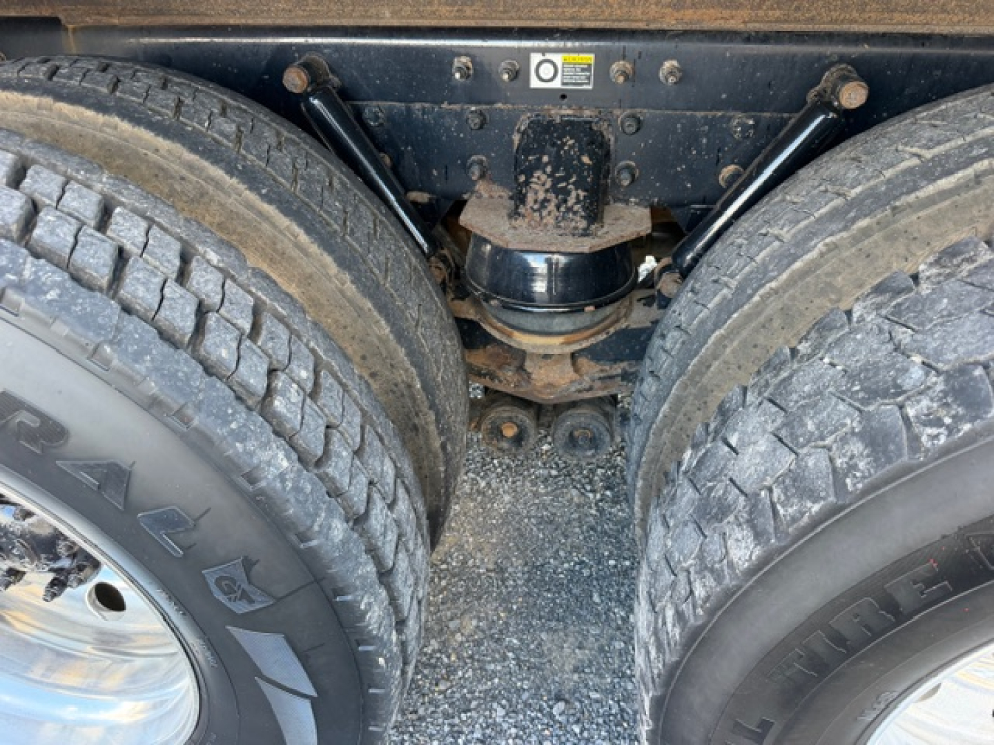 Kenworth T880 rear dual-drive axle with suspension and differential housing; dual tires visible, mud and dirt on components.