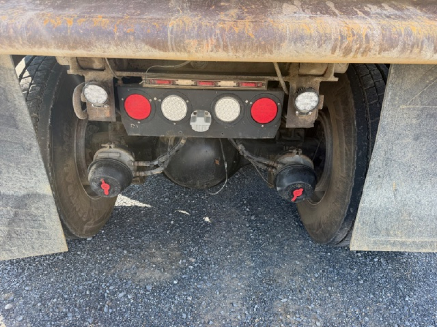 Rear view of Kenworth T880 hitch area with dual wheels, mud flaps, and control panel showing circular gauges on a red/black plate.