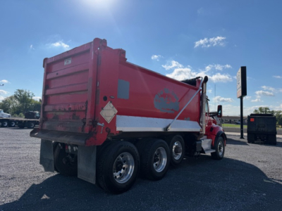 Kenworth T880 dump truck in-yard showing red dump bed and rear wheels, side view with suspension and tires visible.