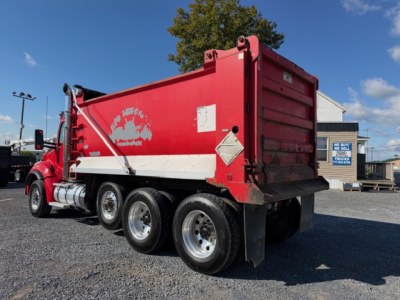 Kenworth T880 dump truck rear and side view showing red dump body with white reflective stripe and dual rear wheels.