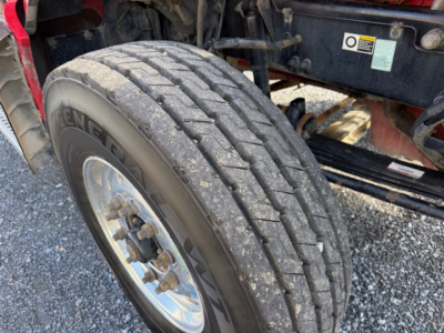 Kenworth T880 wheel and front suspension area with large treaded tire and alloy rim, undercarriage visible.