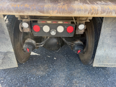 Rear view of Kenworth T880 hitch area with dual wheels, mud flaps, and control panel showing circular gauges on a red/black plate.