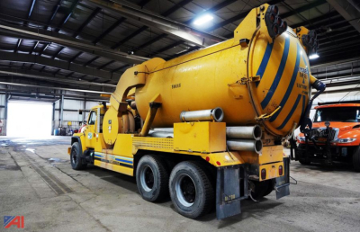 Industrial vacuum truck in a warehouse showing a yellow f1954 vactor jet-rodder with blue stripes and rear jet hoses, 6x4 configuration, built by International