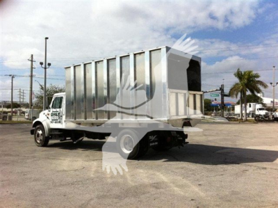 Dump truck with silver cargo bed mounted on white truck chassis, rear view showing open-top cargo area and raised tailgate, dealership lot in background.
