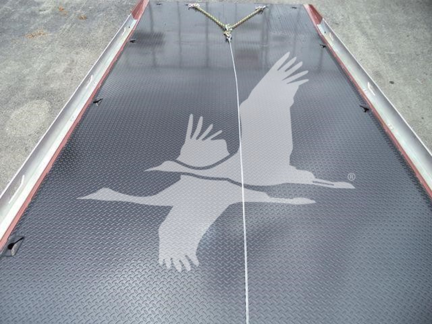 Truck bed with textured black surface featuring a white flying geese decal. Center seam and red edges visible.