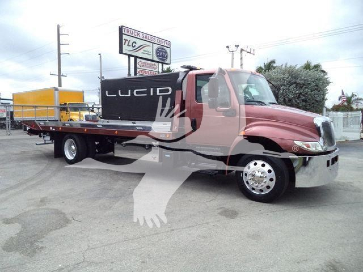 Truck from the side showing a red International MV rollback with a flatbed; license plate not visible; company signage in background.