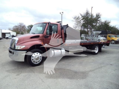 Truck with rollback bed showing red cab and silver flatbed, side view, dealership lot in background.
