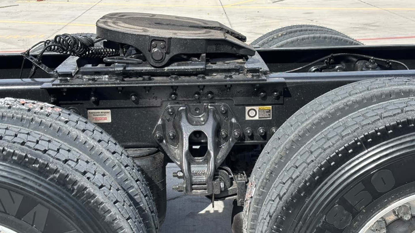 Kenworth T680 chassis and fifth wheel area with dual rear axle and visible hitch, front view showing frame and suspension components.