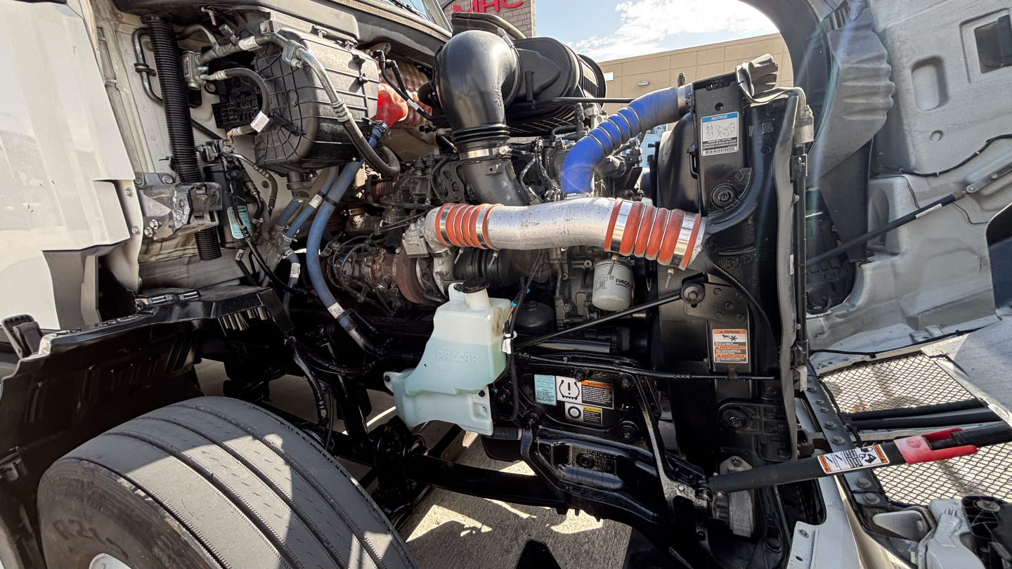 Kenworth T680 engine bay showing coolant reservoir and various hoses with engine components visible.