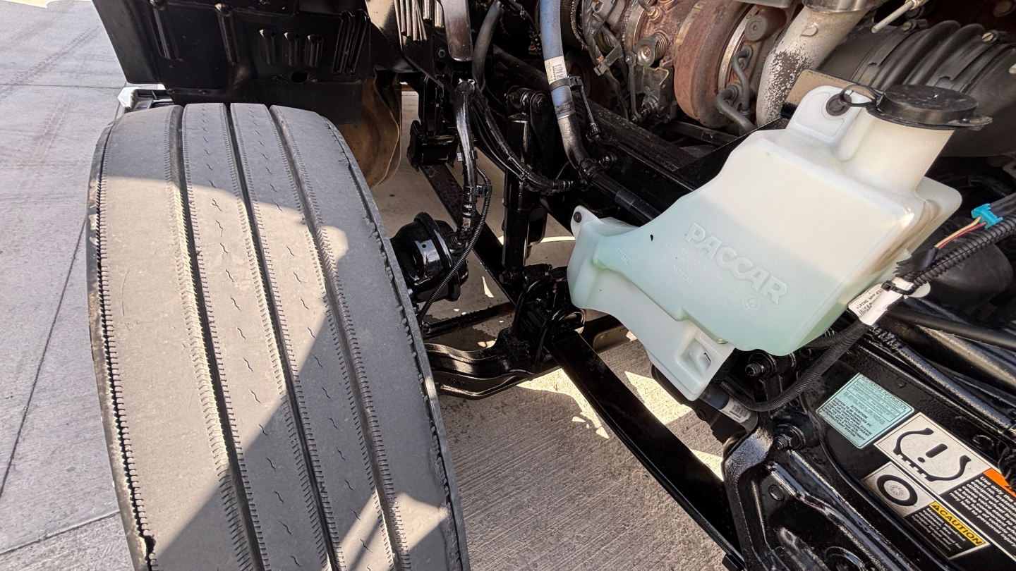 Kenworth T680 engine bay showing coolant reservoir and front fender area with visible hoses and reservoir cap.