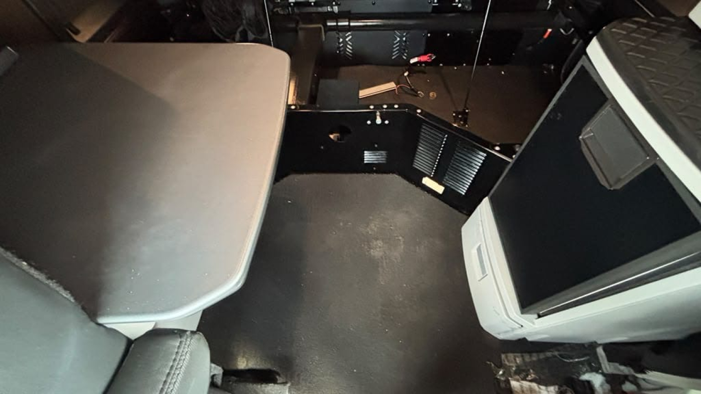 Vehicle interior showing cab seating area and floor with dashboard and storage compartments; no legible labels visible.