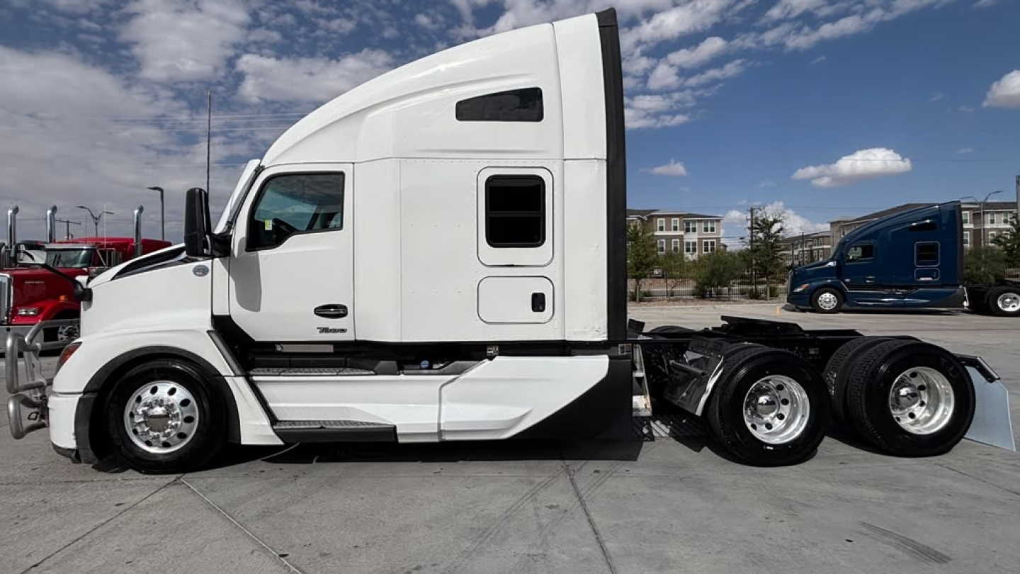 Kenworth T680 side view showing sleeper cab, white exterior, chrome wheels, dual rear axles. No visible text besides generic truck features.