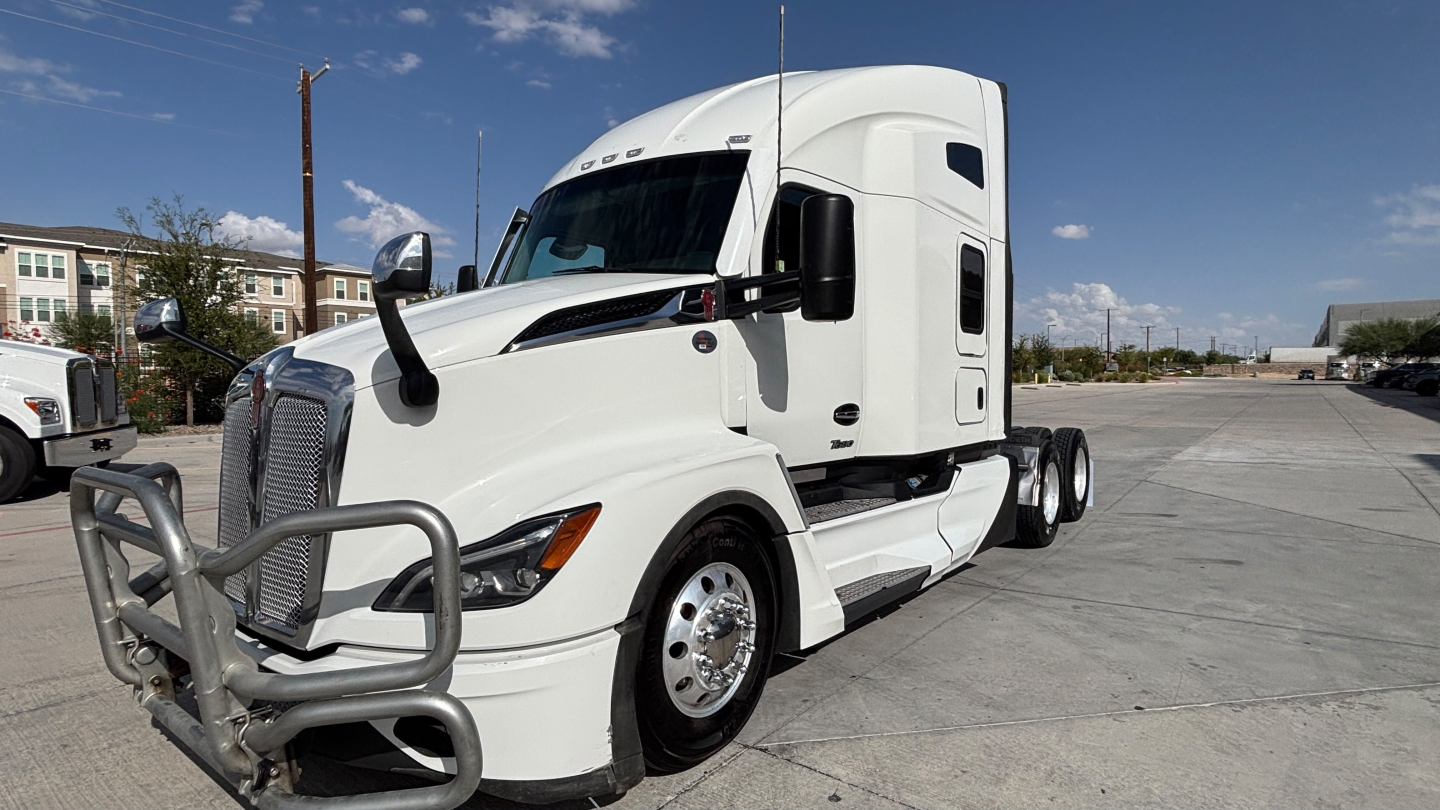 Kenworth T680 truck front-left view showing white cab, protective grille, black mirrors, and sleeper cab with chrome wheel covers.