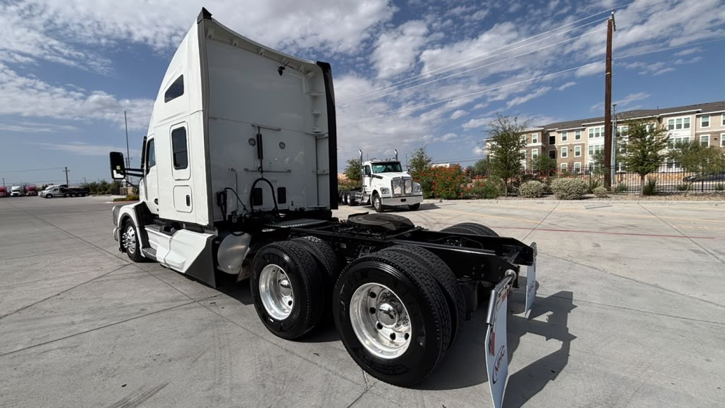 Truck chassis and cab of a 2023 Kenworth T680, rear view showing dual rear axles, tires, and white sleeper cab.