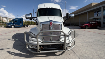 Kenworth T680 conventional sleeper truck front view with grille guard and chrome bumper, white paint, parking lot backdrop.