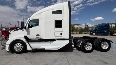 Kenworth T680 side view showing sleeper cab, white exterior, chrome wheels, dual rear axles. No visible text besides generic truck features.